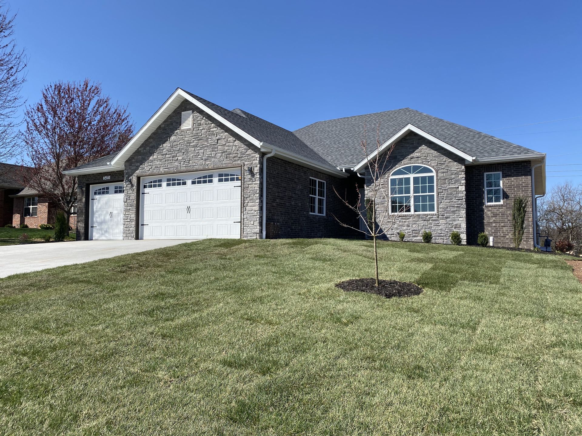 A brick house with a white garage door and a tree in front of it.