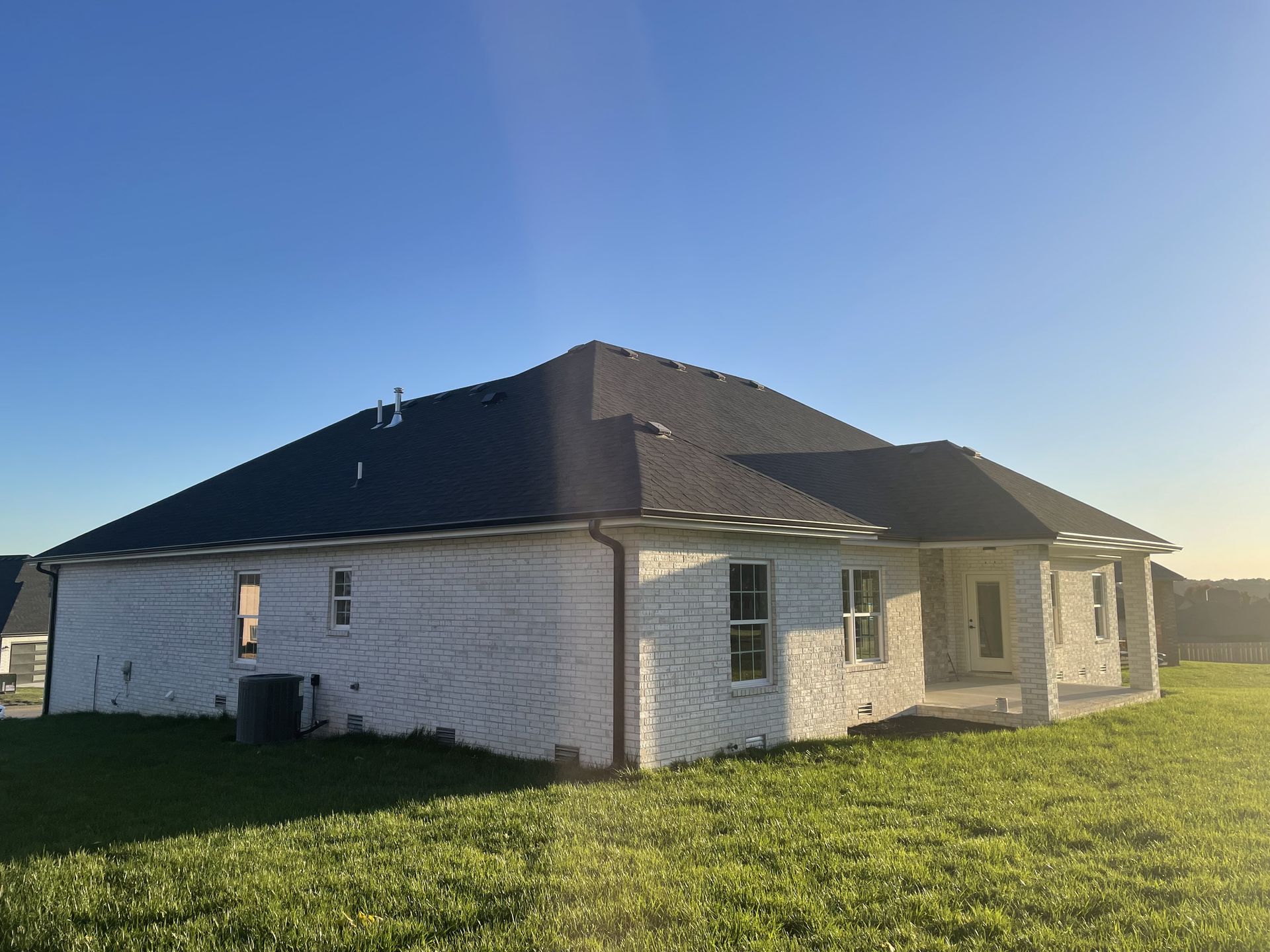 A white house with a black roof is sitting on top of a lush green field.