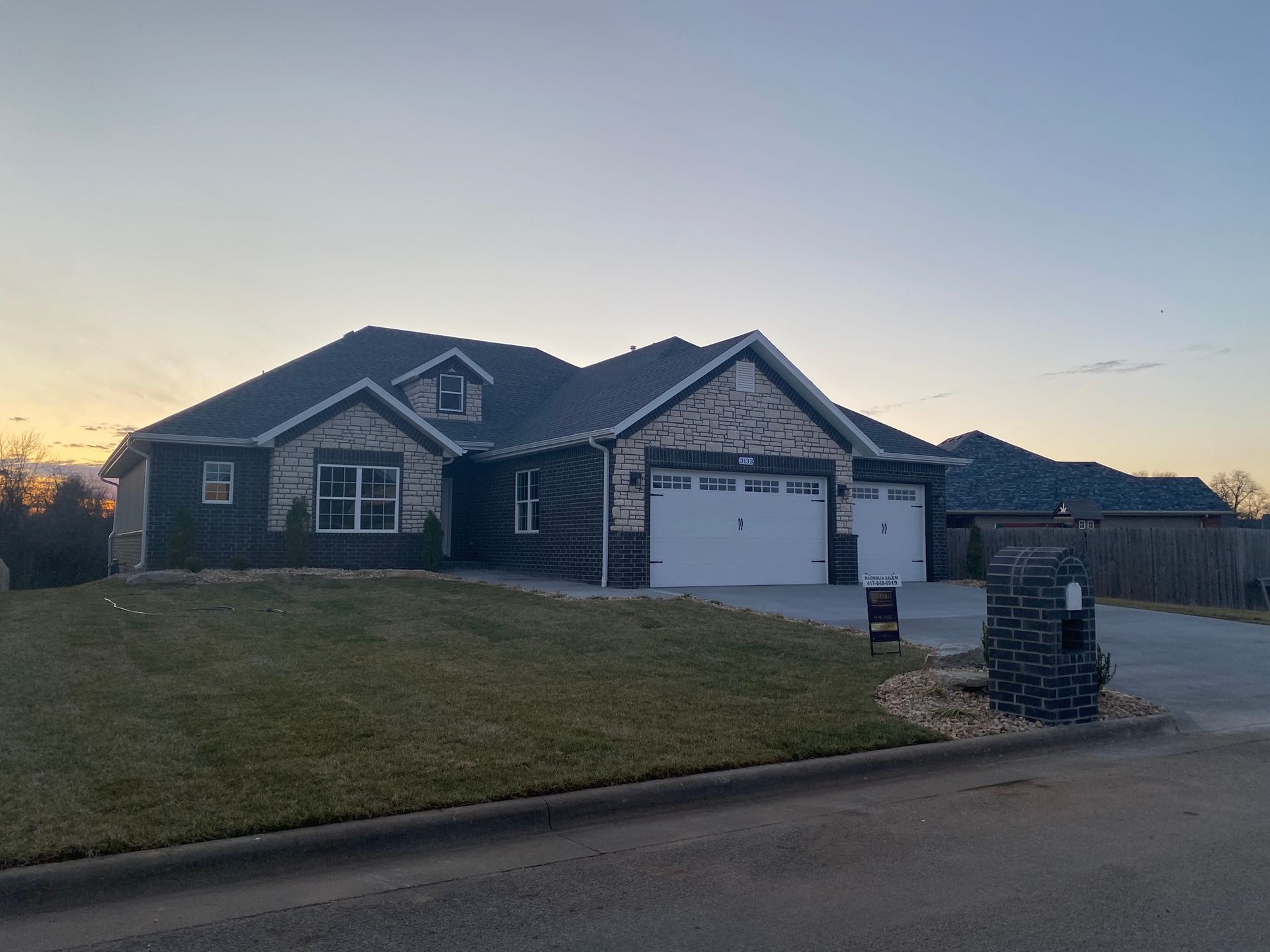 A large house with a gray roof and a white garage door is sitting on top of a lush green lawn.