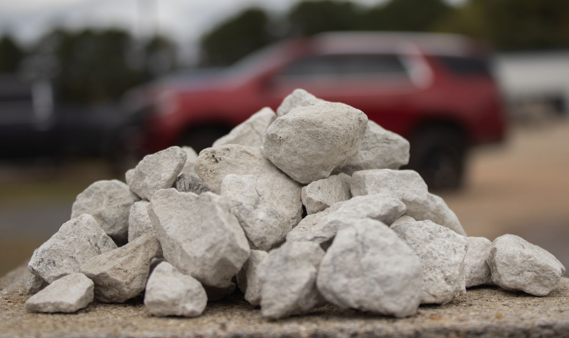 A pile of rocks with a red suv in the background.
