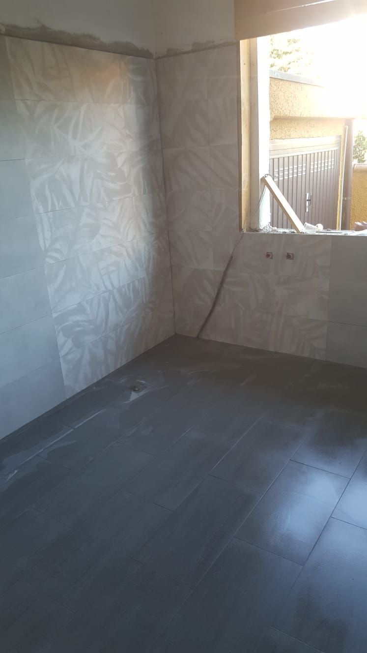 Stanza vuota con pareti piastrellate e pavimento grigio, finestra sulla destra.