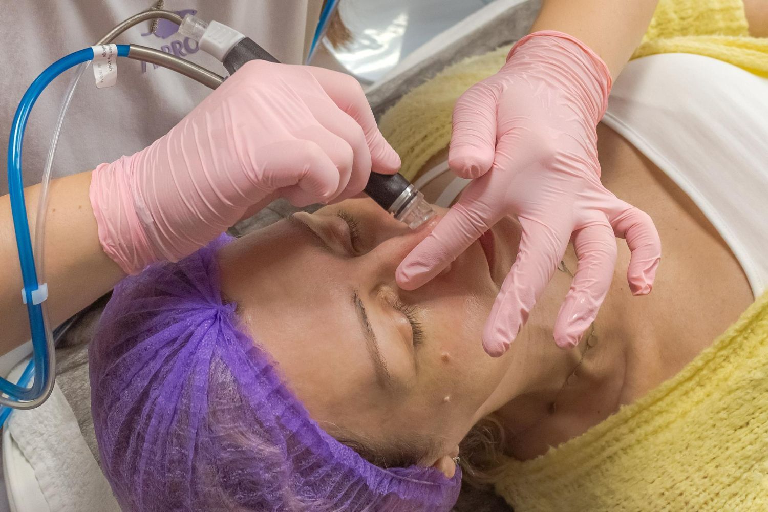 Person receiving facial treatment with gloved hands using a device.