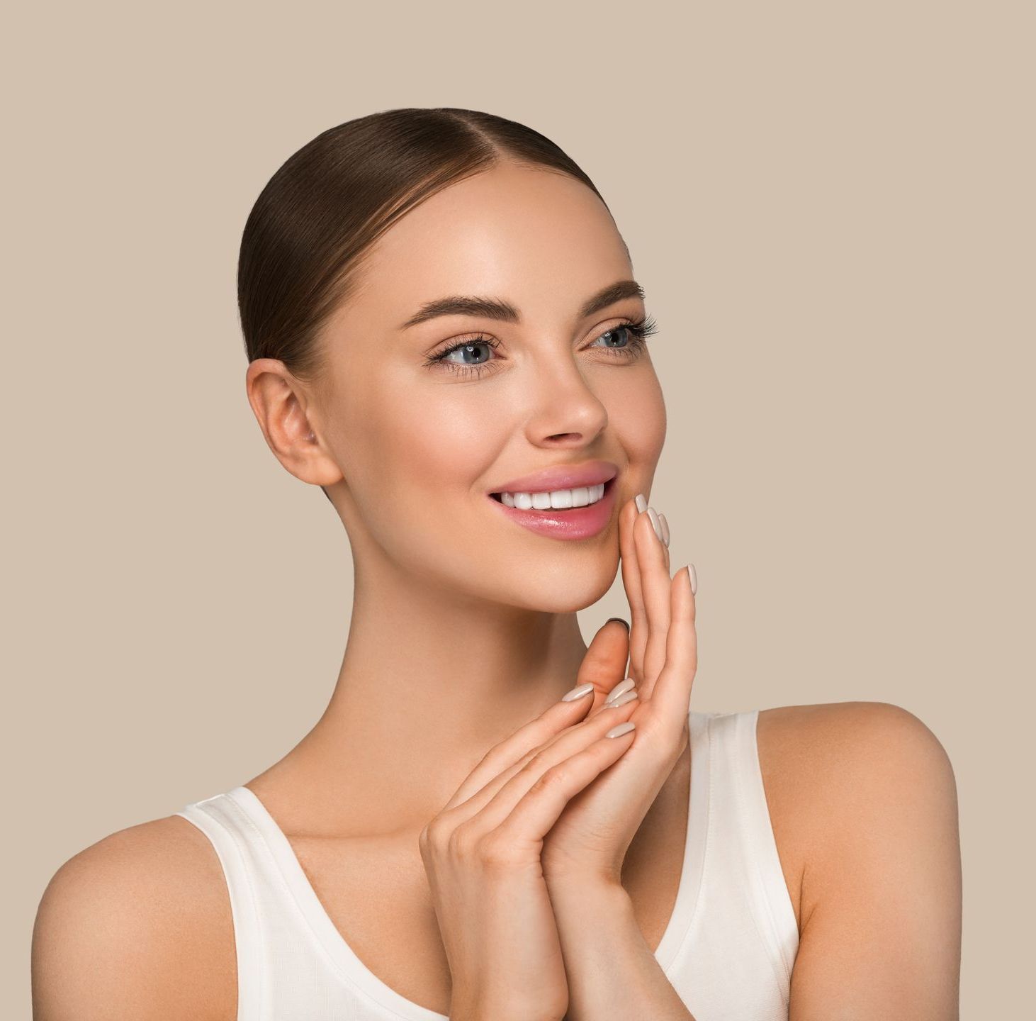 A woman is smiling and touching her face with her hands.