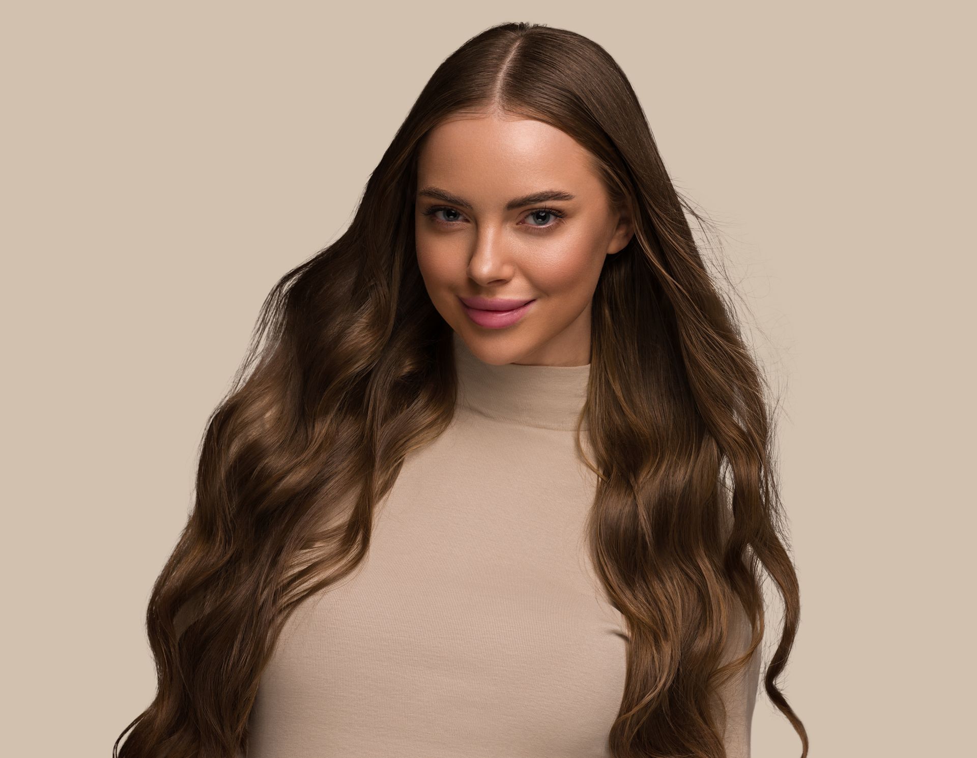 A woman with long brown hair is wearing a beige sweater and smiling.