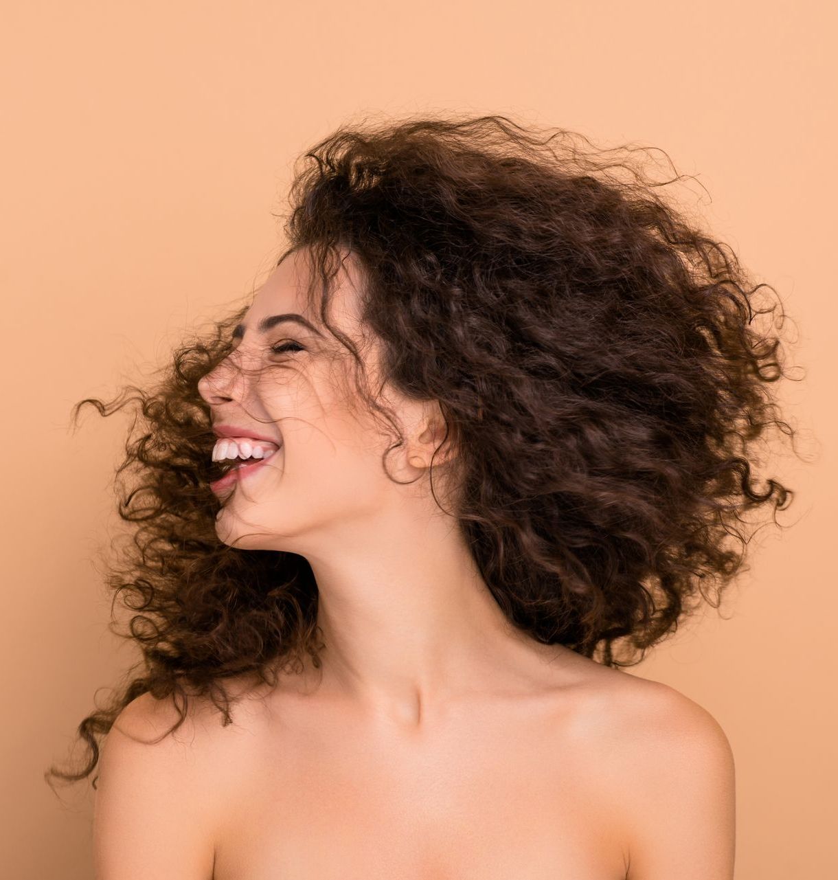 A woman with curly hair is smiling with her hair blowing in the wind.
