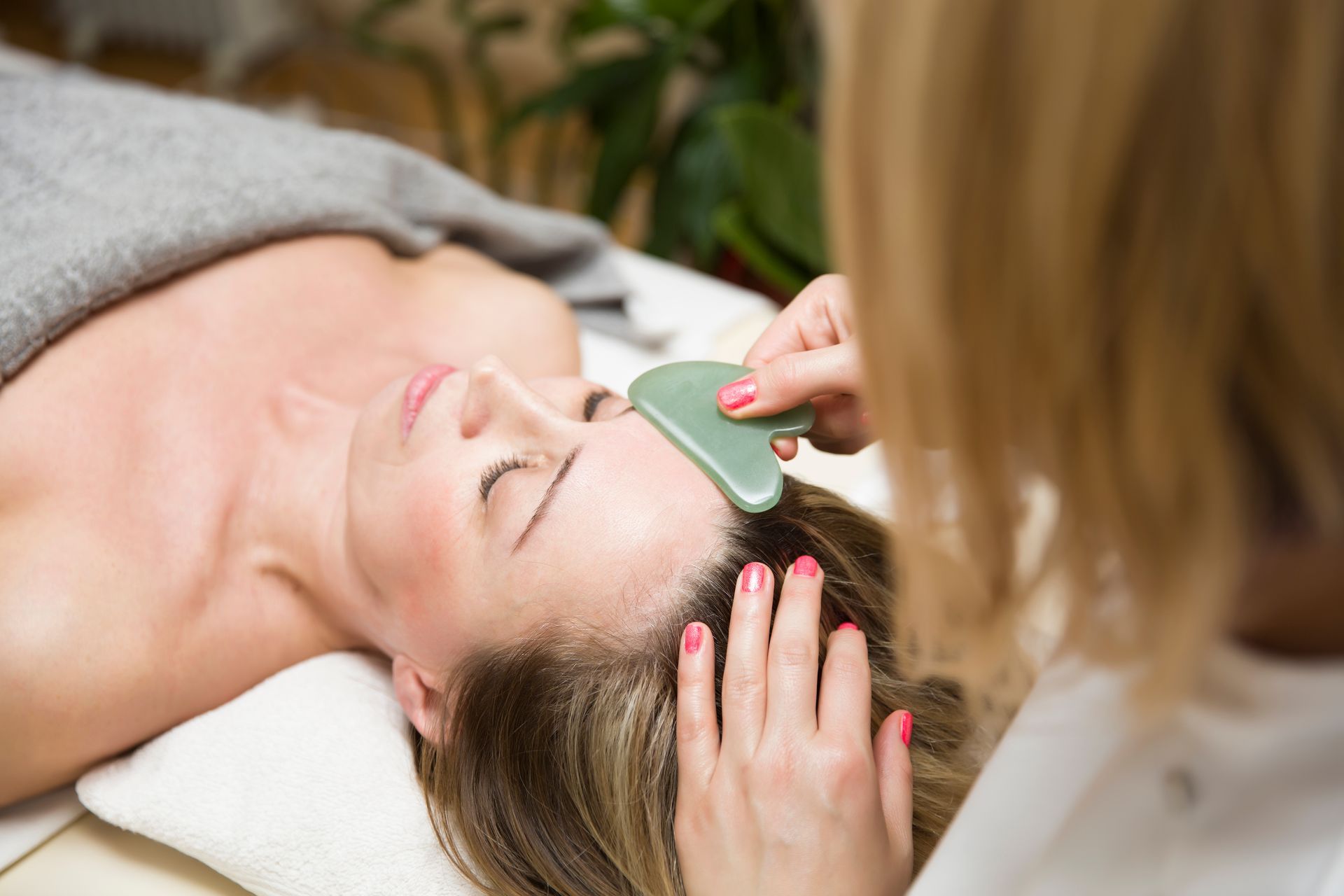 A woman is getting a gua sha treatment on her face.