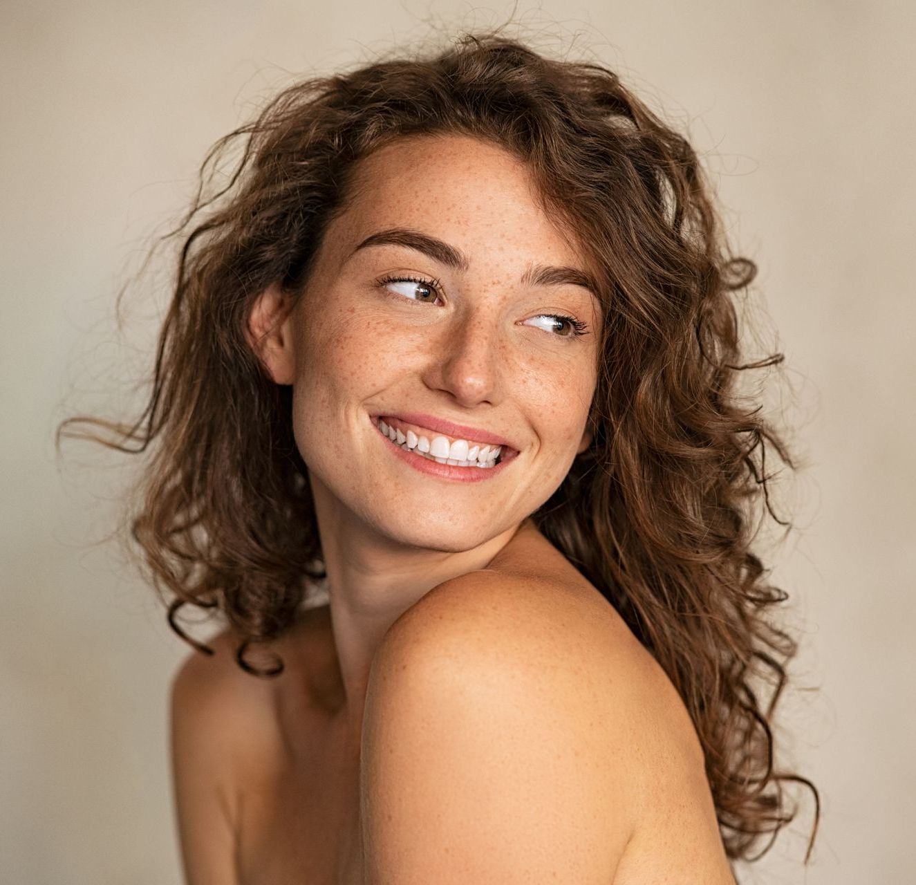 A woman with curly hair is smiling and looking over her shoulder.