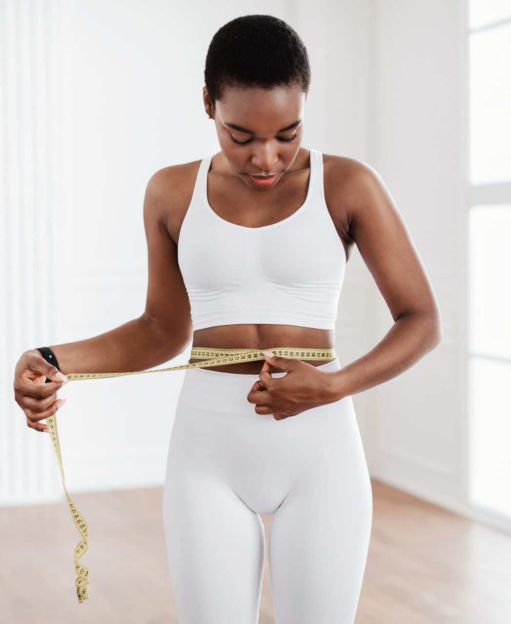 A woman is measuring her waist with a tape measure.