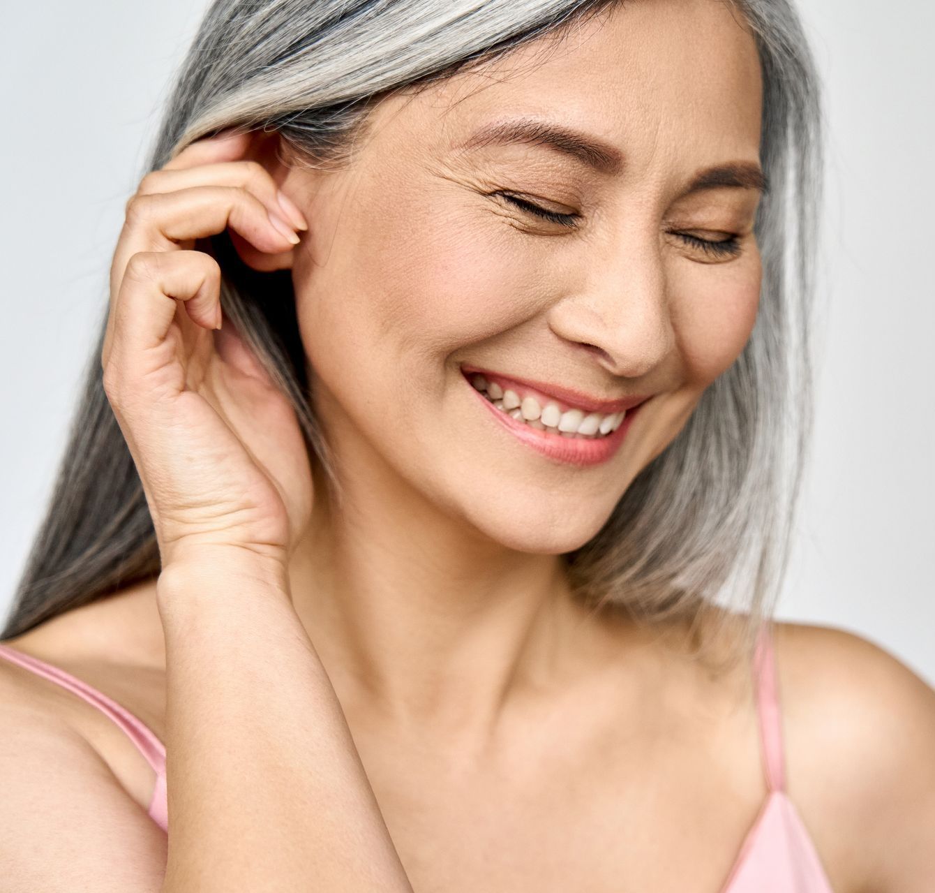 A woman with gray hair is smiling and touching her hair.