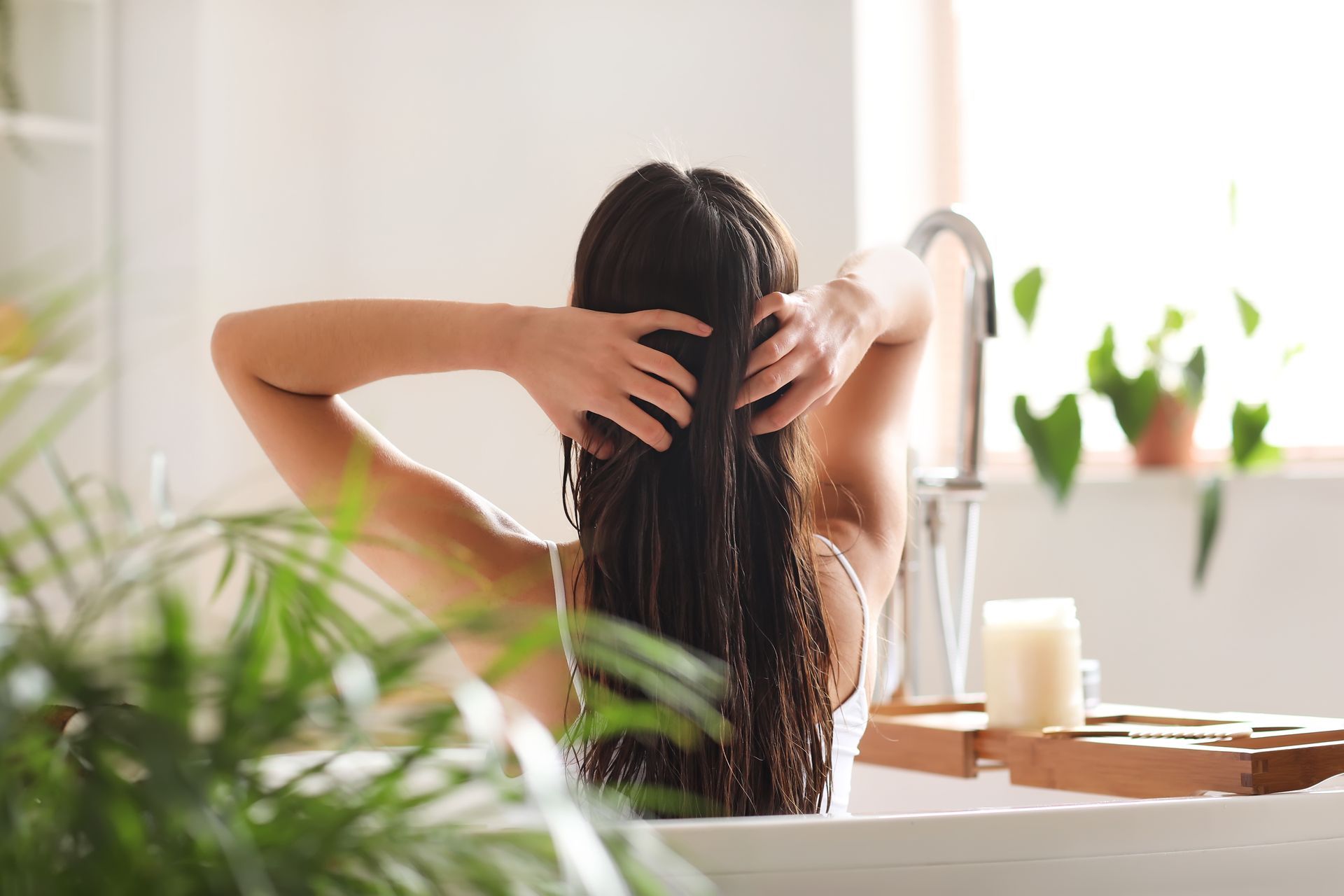 A woman is taking a bath in a bathtub and touching her hair.