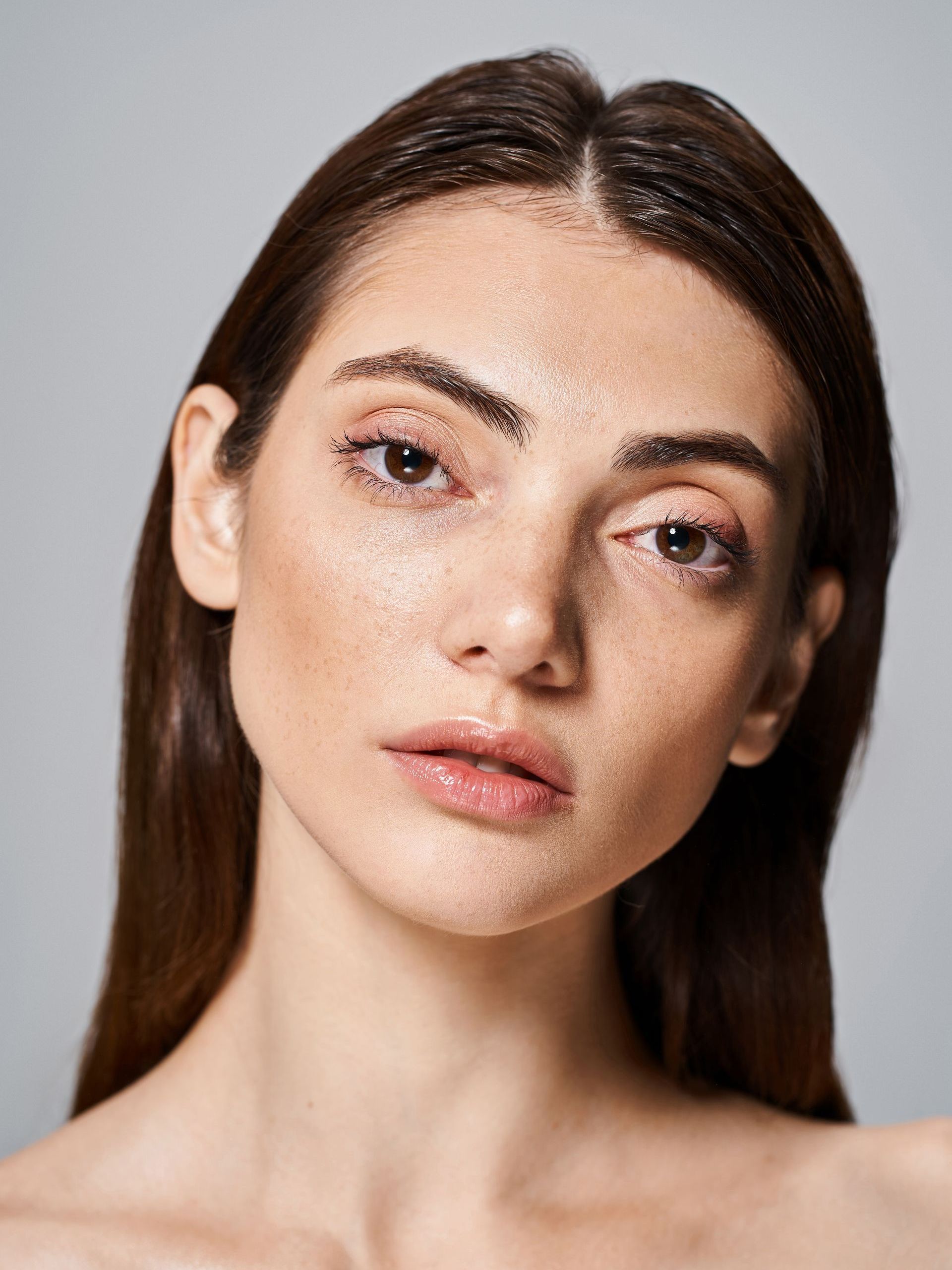 A close up of a woman 's face with wet hair on a gray background.