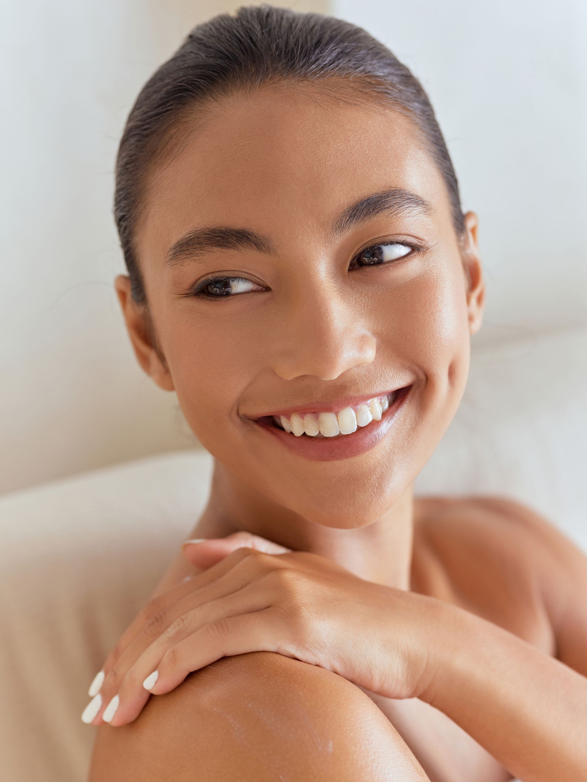 A woman is smiling and touching her shoulder while sitting in a bathtub.