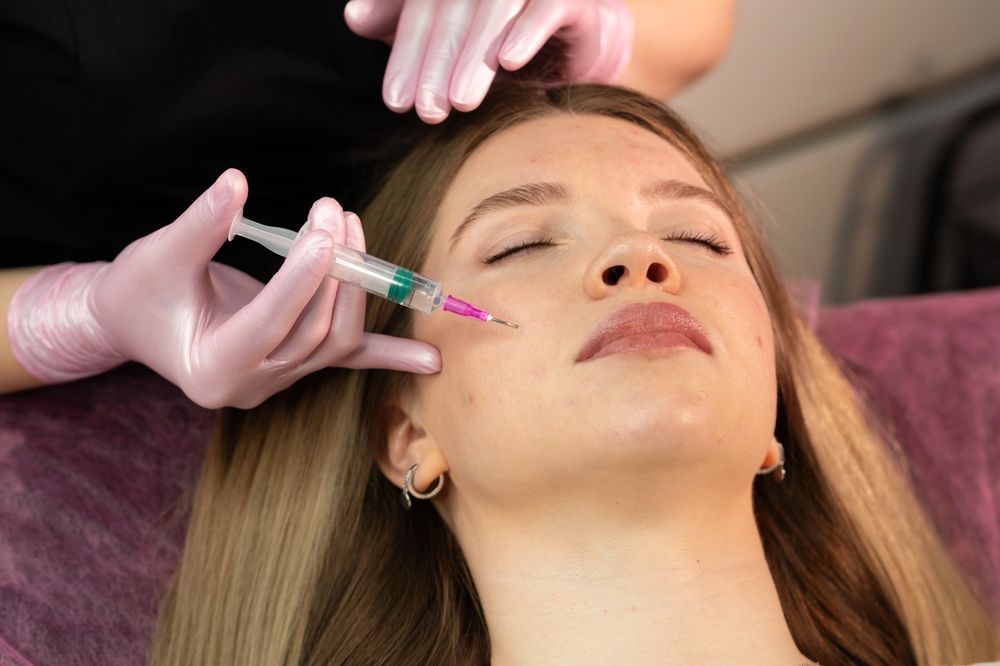 Person receiving a facial injection. A medical professional in pink gloves injects a syringe into the person's cheek.