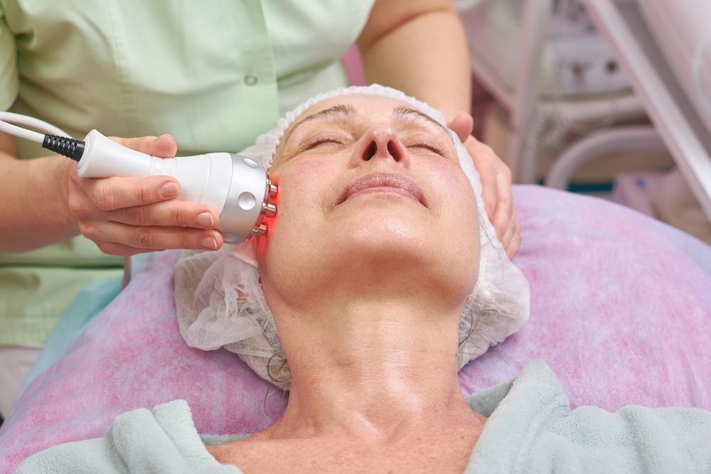 Woman receiving a facial treatment with a red light device.