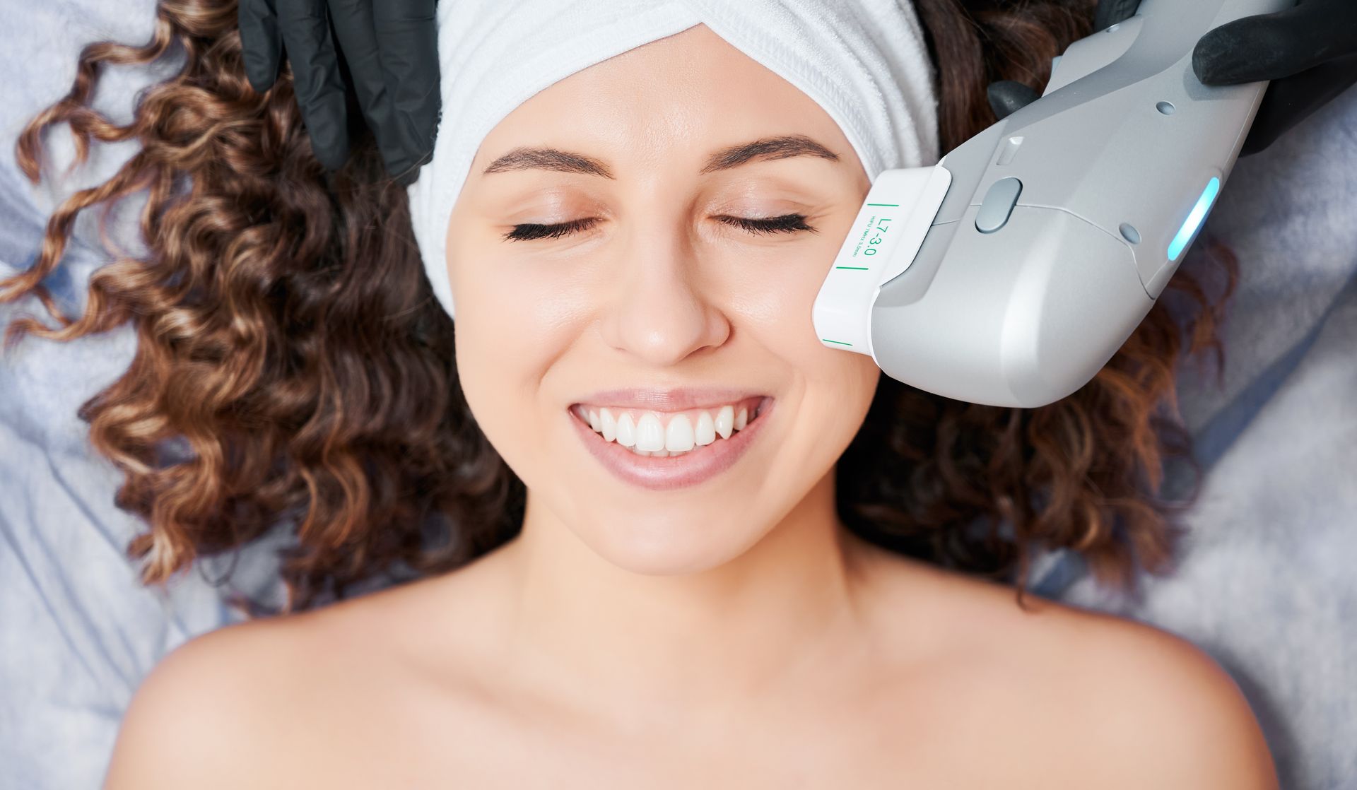 A woman is smiling while getting an ultrasound treatment on her face.
