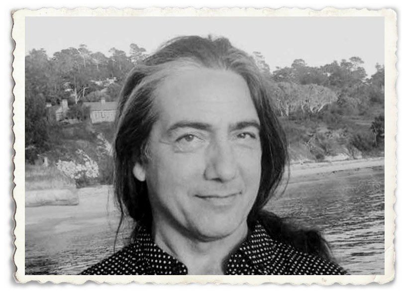 A man with long hair is smiling in a black and white photo