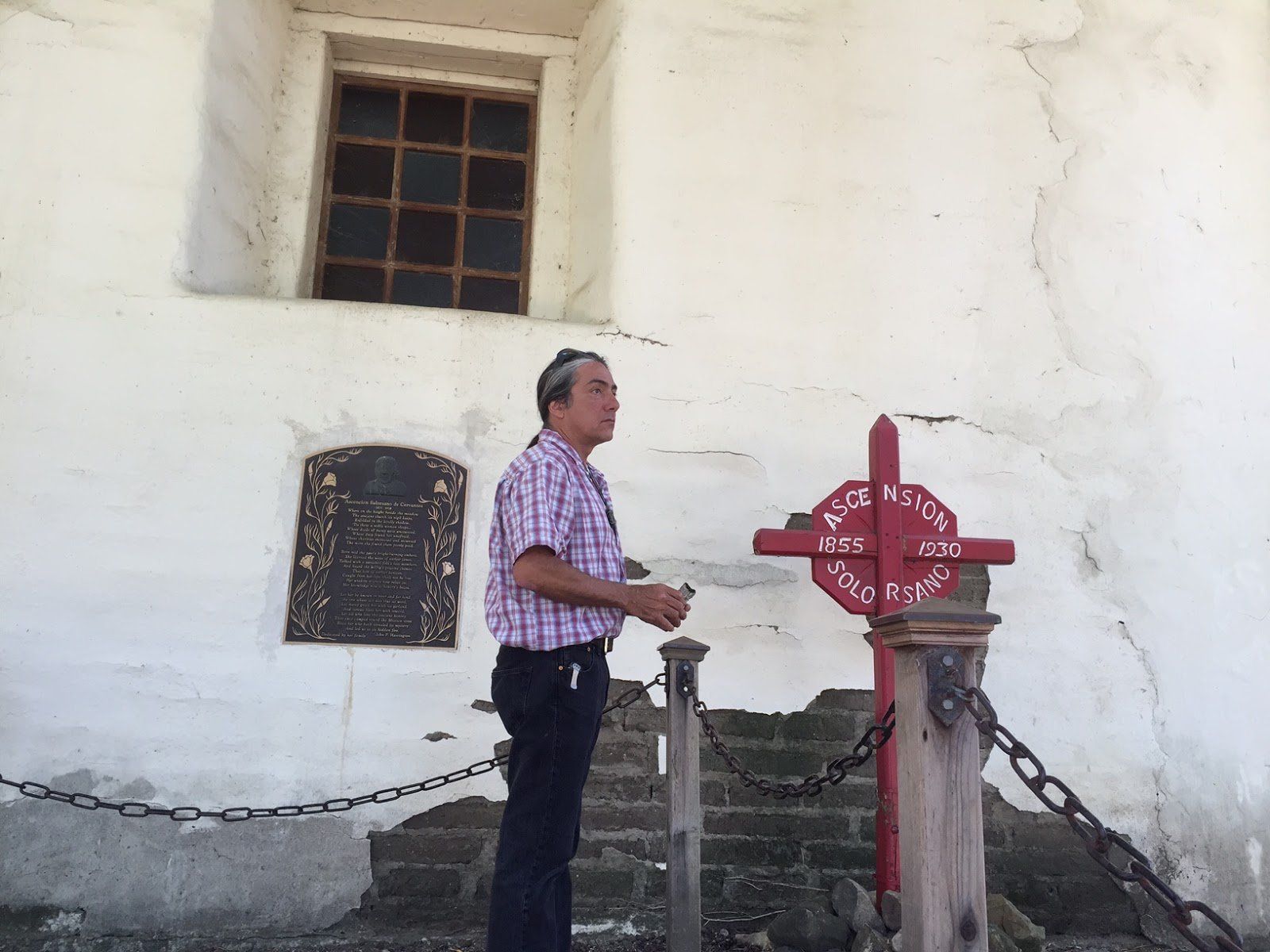 A man in a plaid shirt stands next to a red cross
