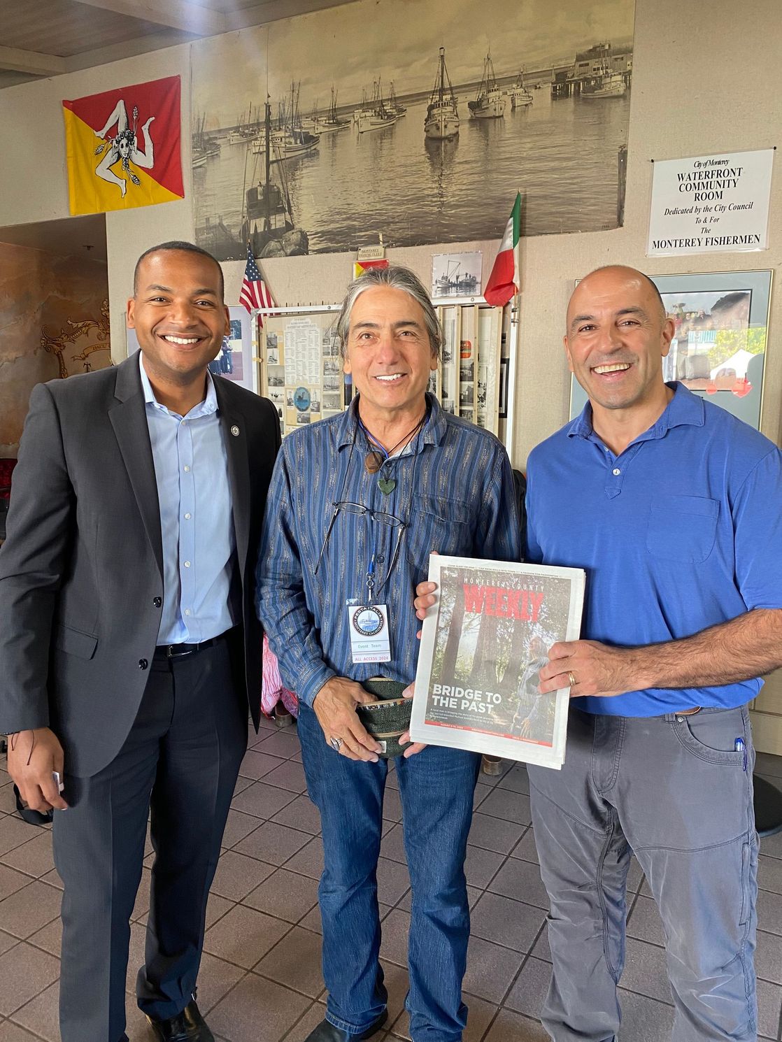 Three men are standing next to each other in a room holding a picture.