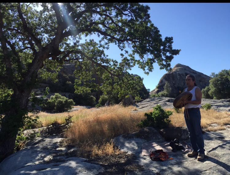 A man playing a drum in a field with a mountain in the background