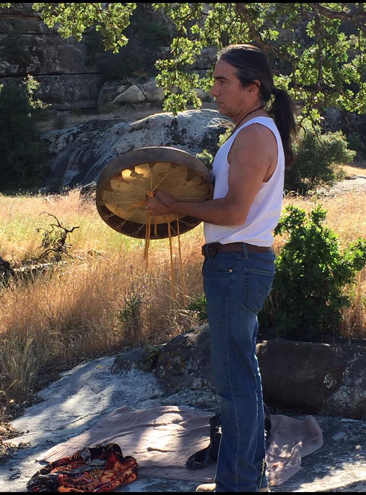 A man in a white tank top is holding a drum in a field.