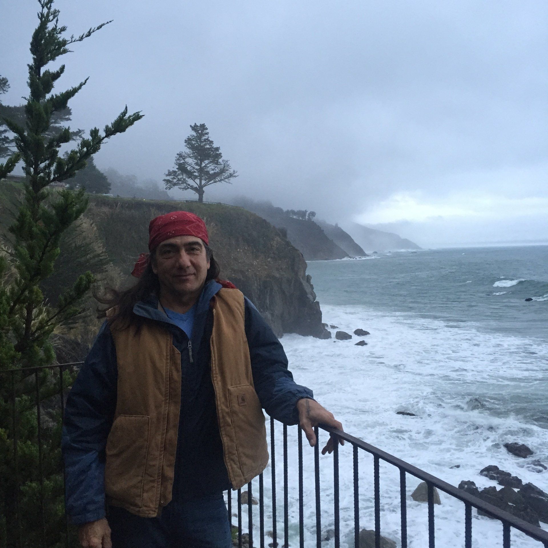 A man standing on a railing overlooking the ocean