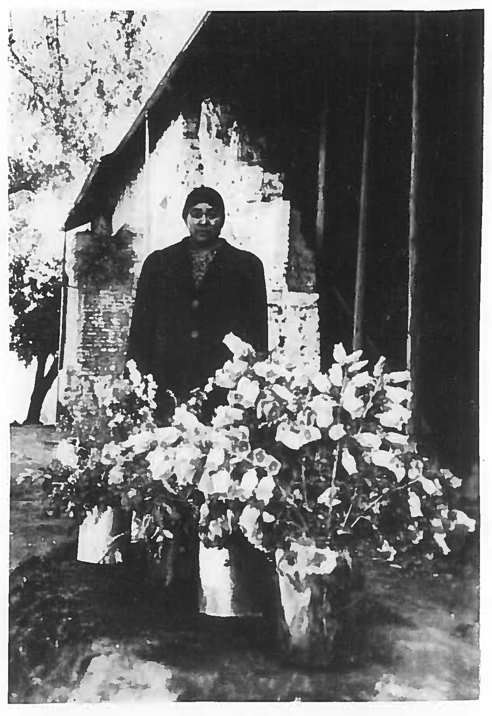 A black and white photo of a man standing in front of potted flowers