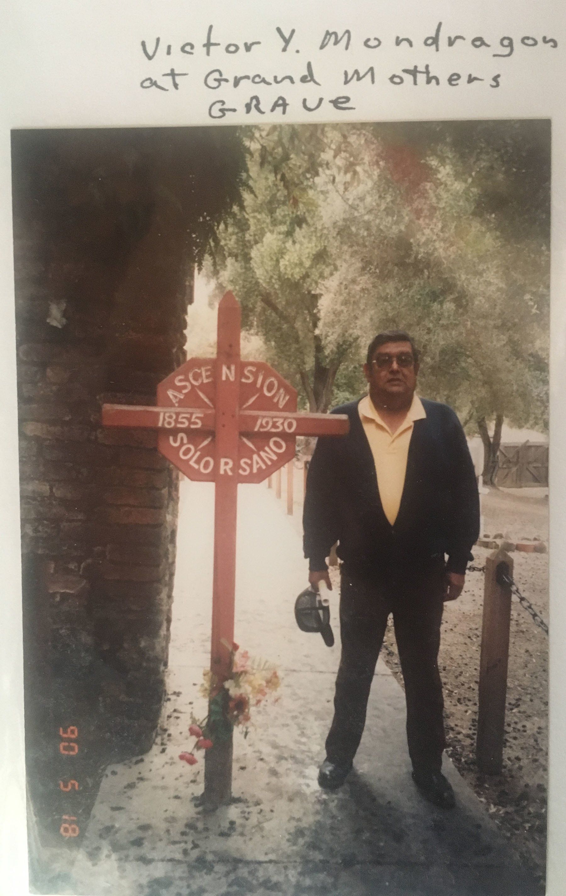 A man standing in front of a cross that says victor y mundragen at grand mothers grave