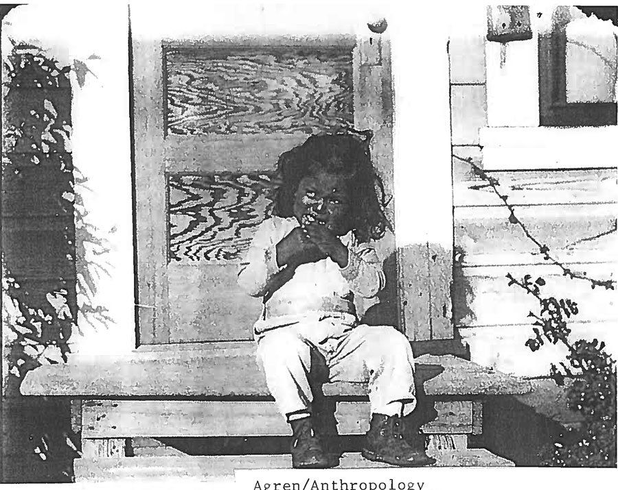 A black and white photo of a child sitting on a porch
