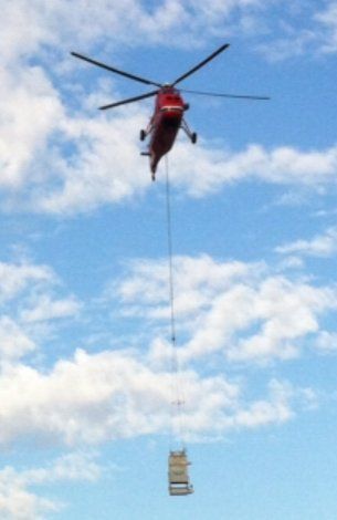 Red helicopter flying while carrying equipment — Little Rock, AR — BM Mechanical Corp. Inc.