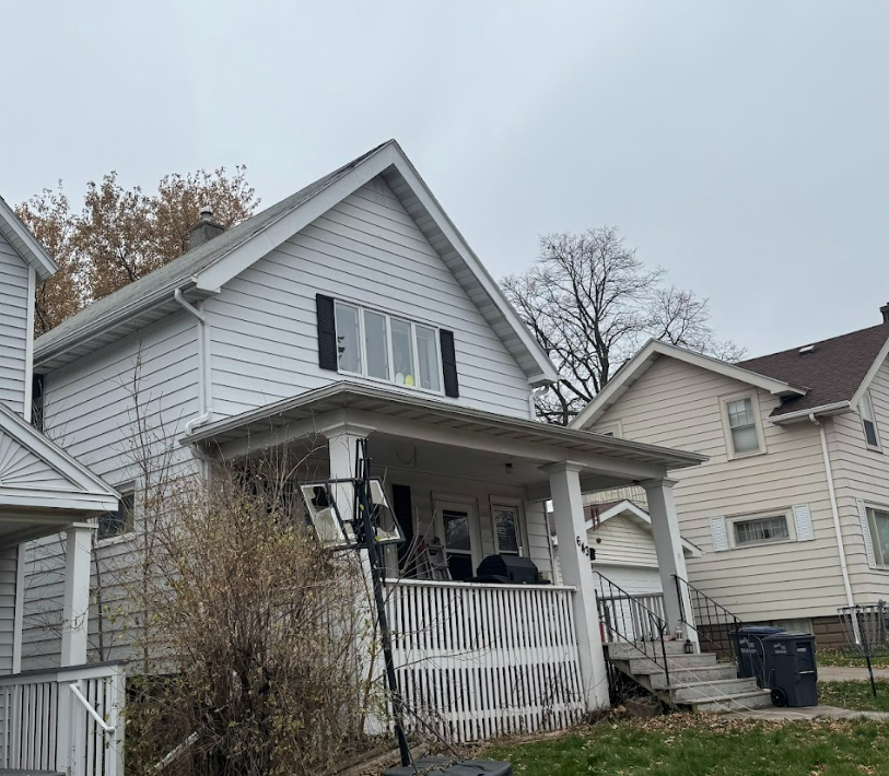 A light-colored two-story house with a front porch, a gabled roof, and a basketball hoop in the yard.