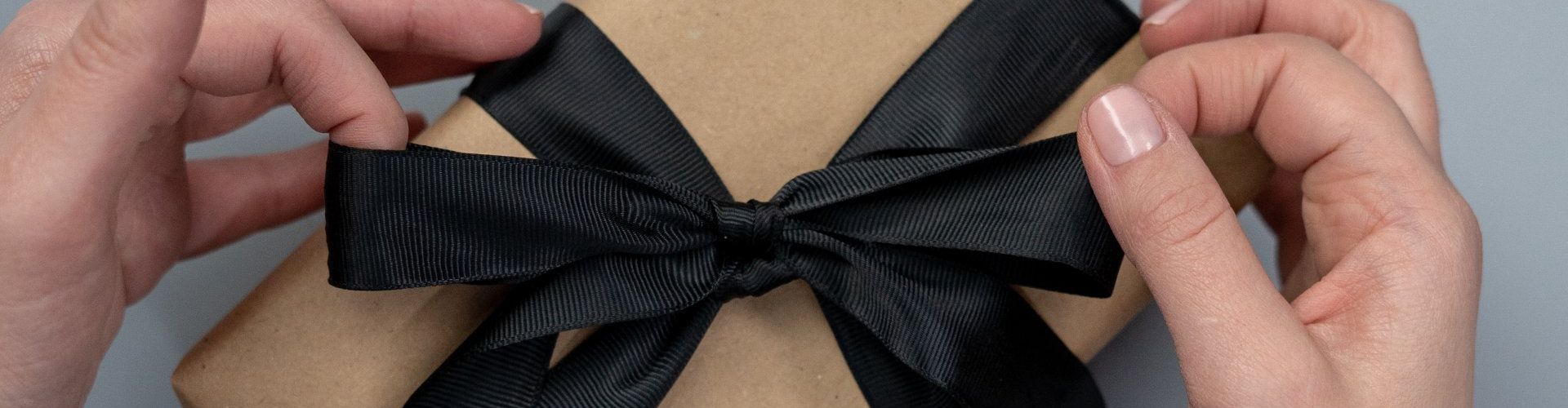a person is holding a gift wrapped in brown paper with a black bow