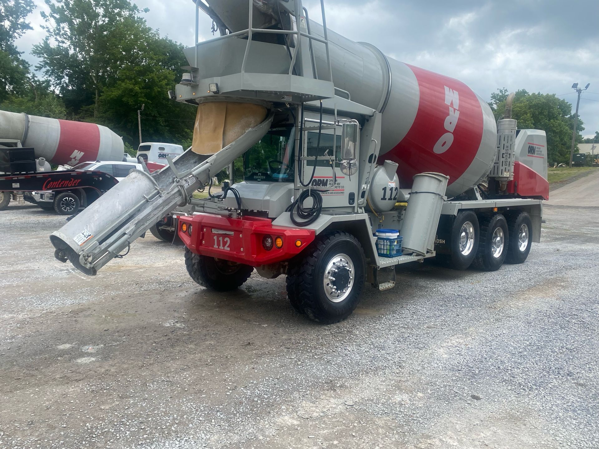A white and red concrete mixer truck parked on a gravel lot with its discharge chute extended.
