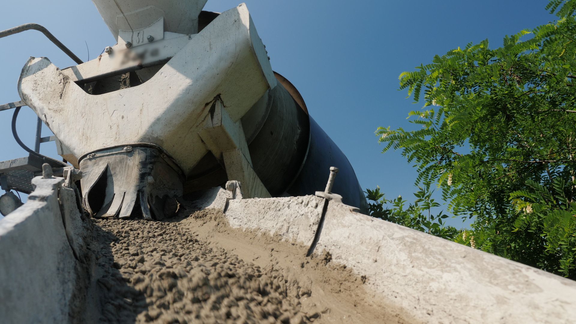 Cement mixer pouring wet concrete onto a construction site under a blue sky