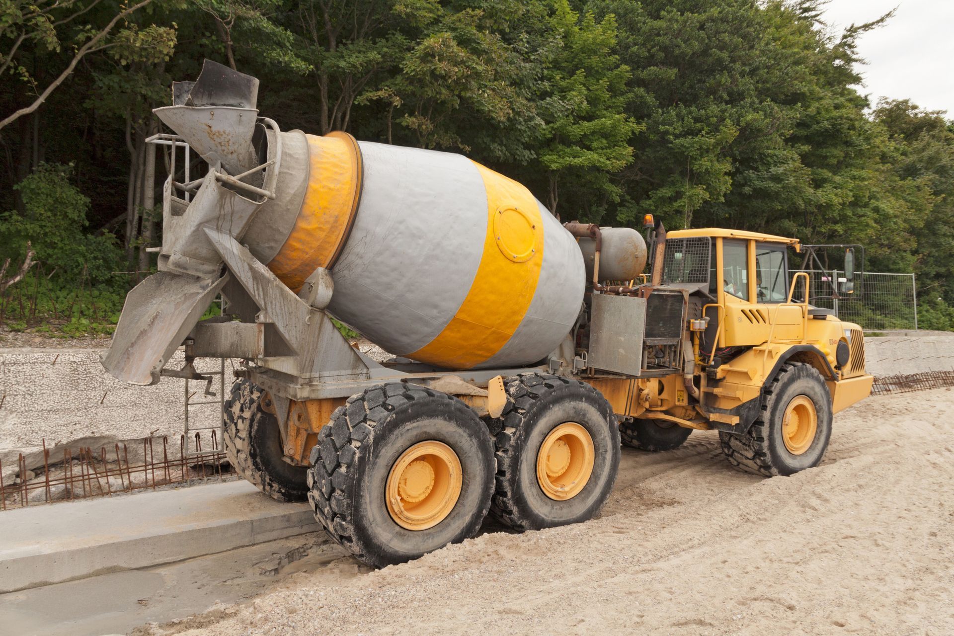 A yellow and gray concrete mixer is parked on a dirt road.
