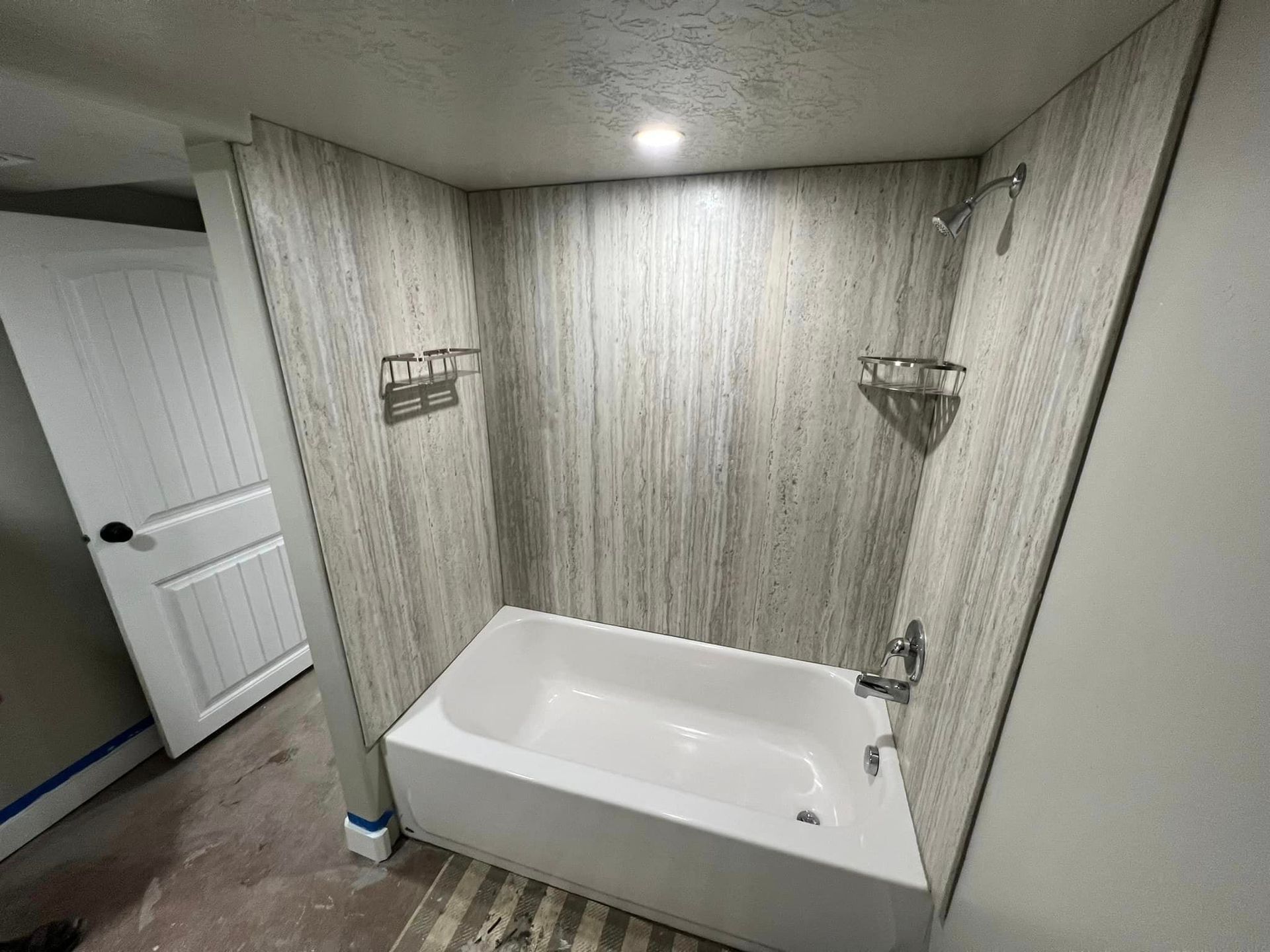 Small bathroom with a white tub, gray wood-look walls, and a ceiling light.