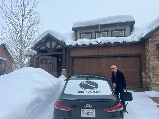 Man in front of a snow-covered home; car in front has business logo, snow-filled driveway.