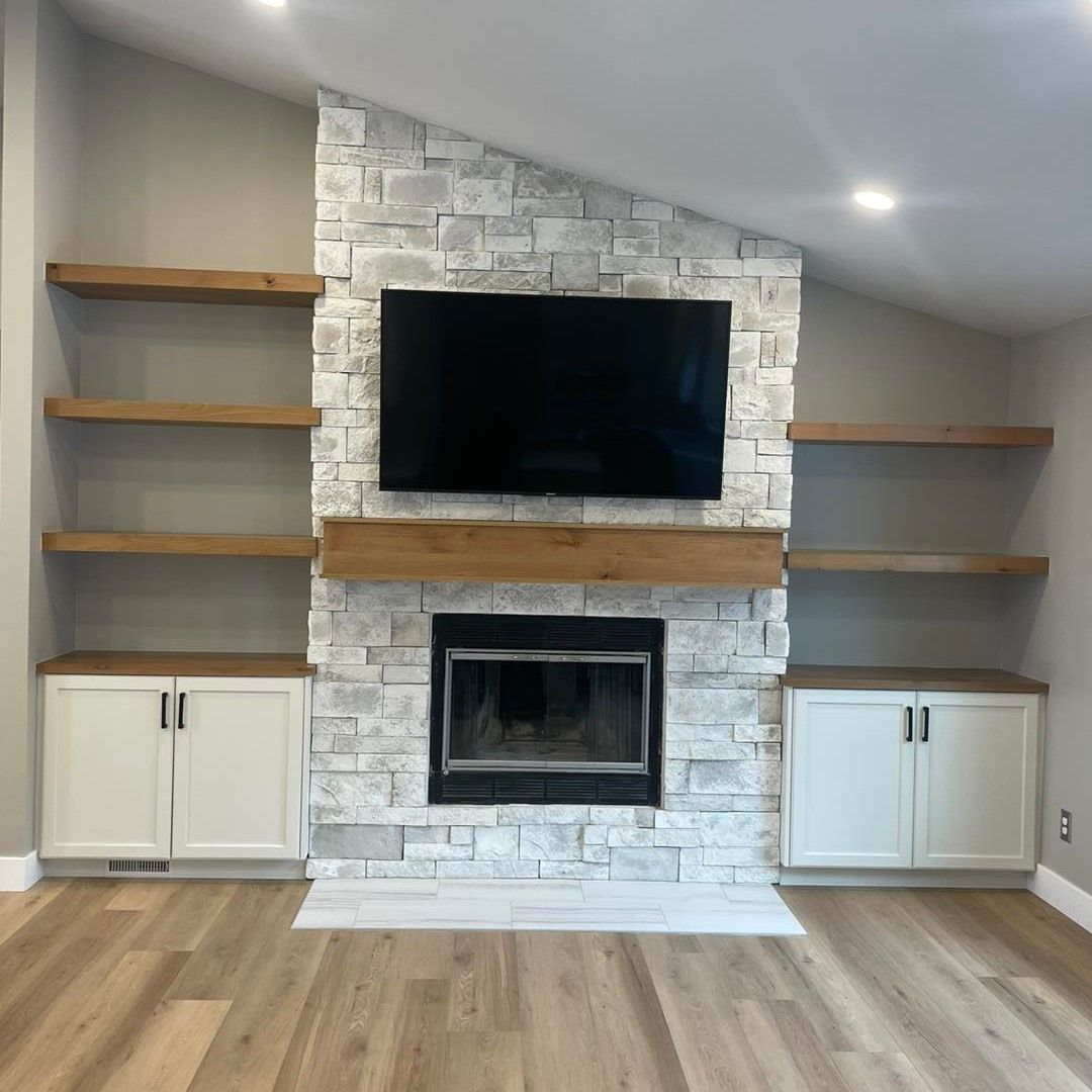 Living room with fireplace, TV, white stone, wood shelves and cabinets, and wood floors.
