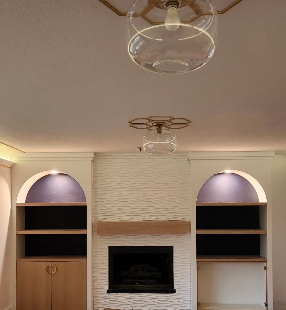 Living room with fireplace, built-in shelves, gold light fixtures, and white walls.