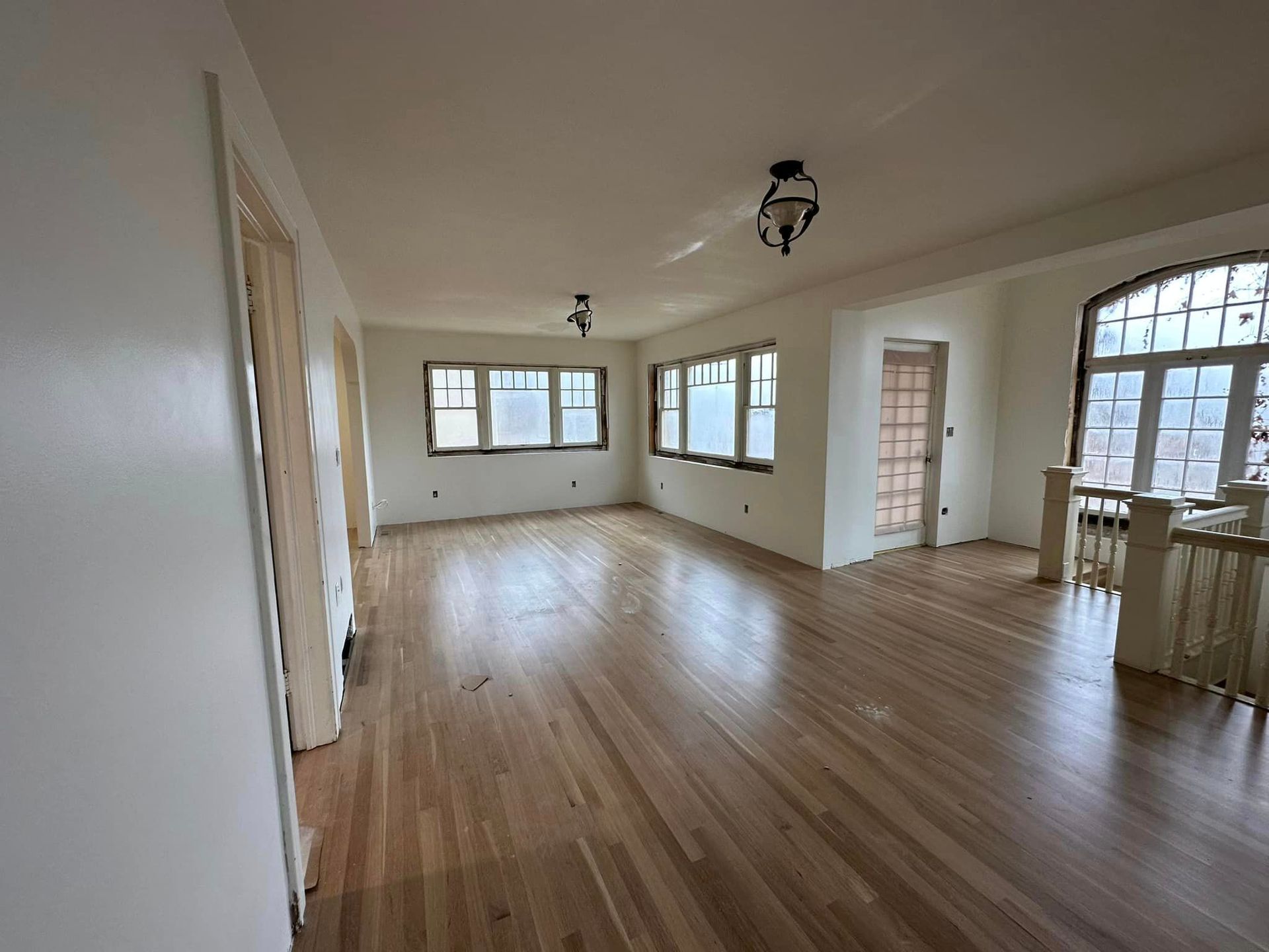 Spacious empty room with wood floors, large windows, and white walls.