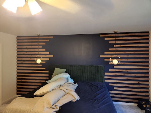 Bedroom with blue wall, wood slat accents, gold pendant lights, and unmade bed.