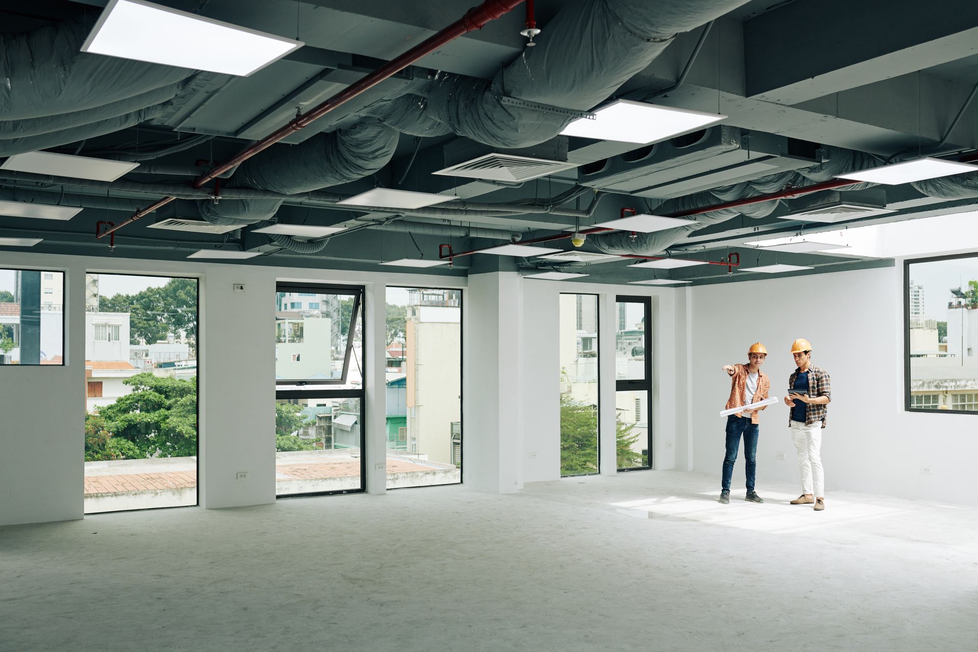 Two men in hard hats are standing in an empty office building.