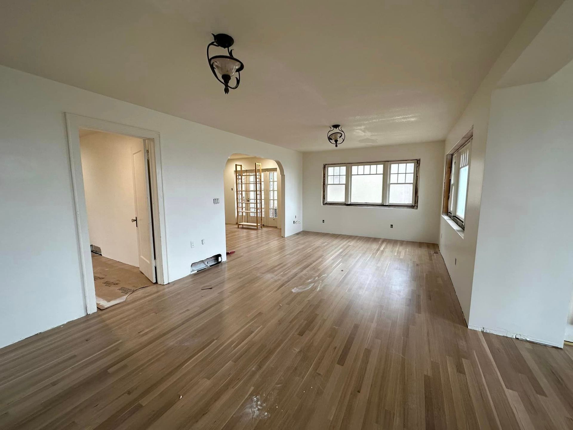 Empty living room with hardwood floors, white walls, and windows letting in natural light