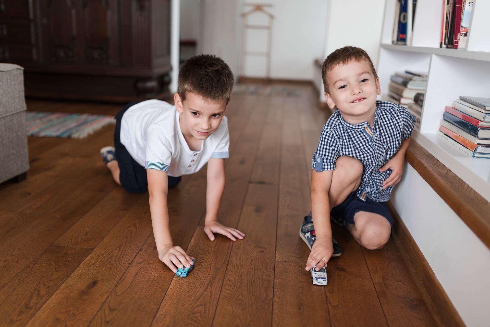 Two children playing with toy cars on a wooden floor in a living room