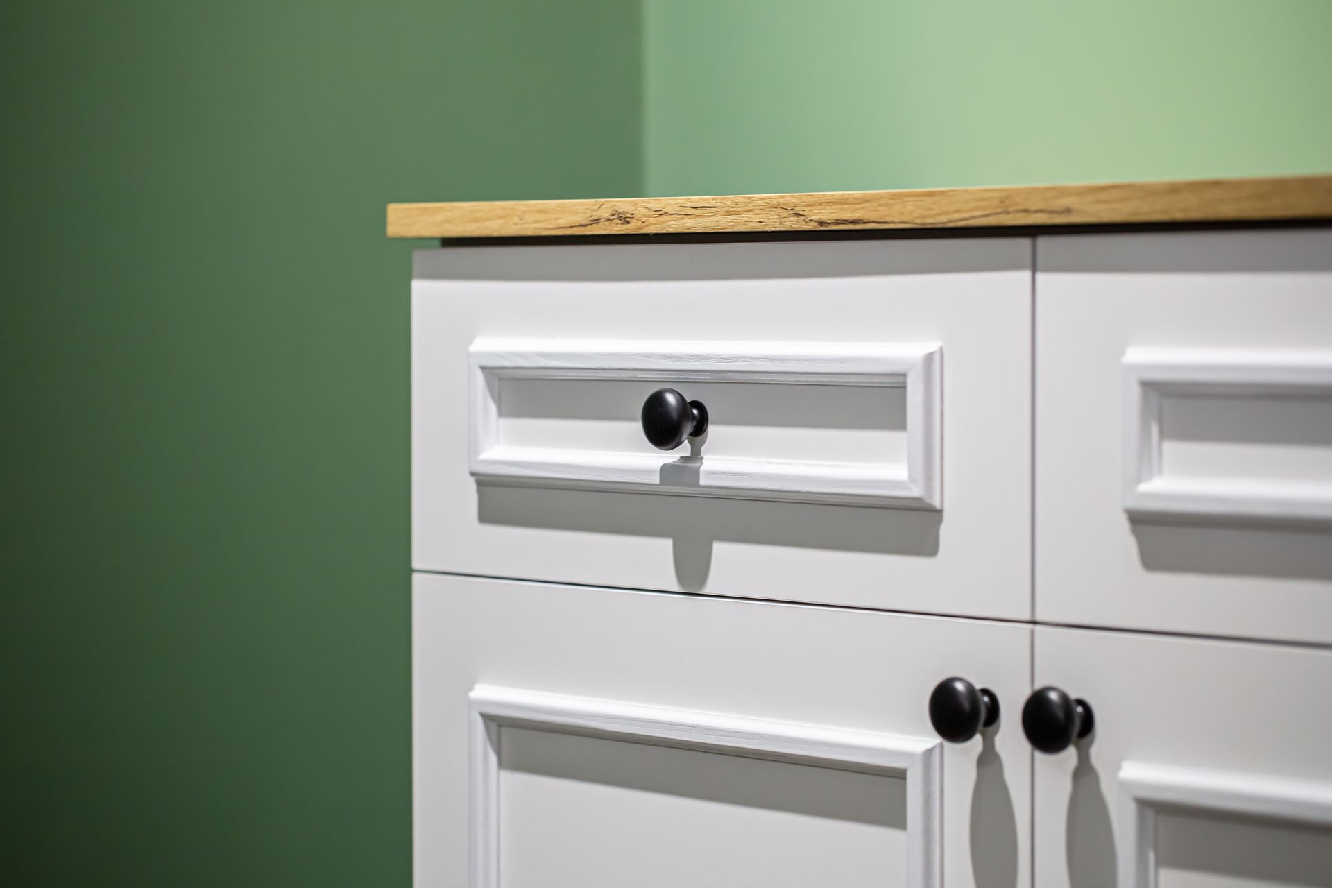 White cabinet with black knobs against a green wall, topped with a wooden countertop