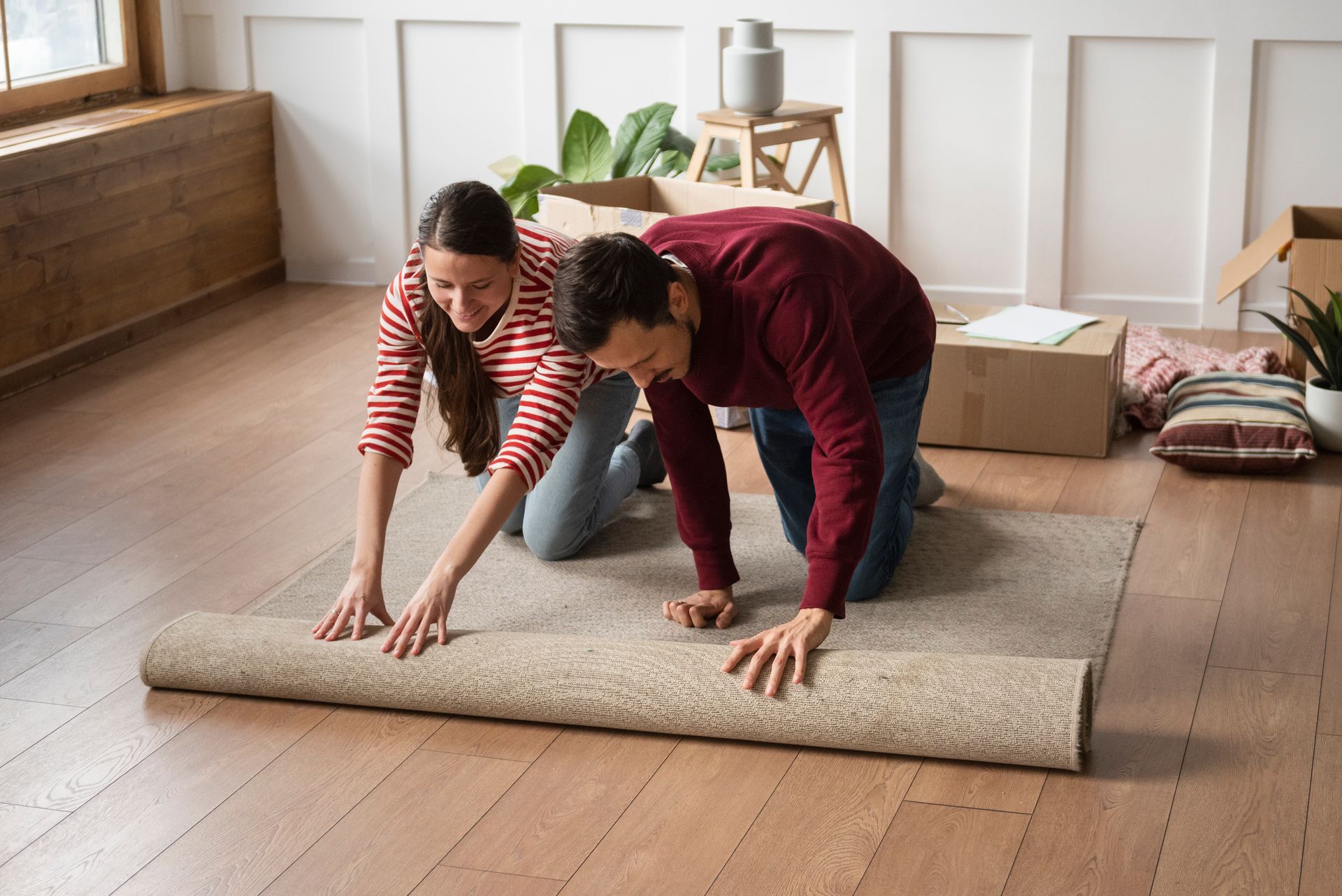 A man and a woman are rolling a rug on the floor.