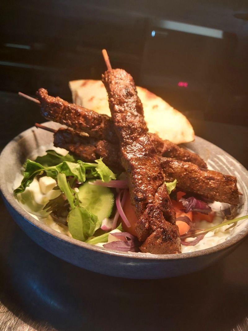 A bowl of food with meat and vegetables on a table.