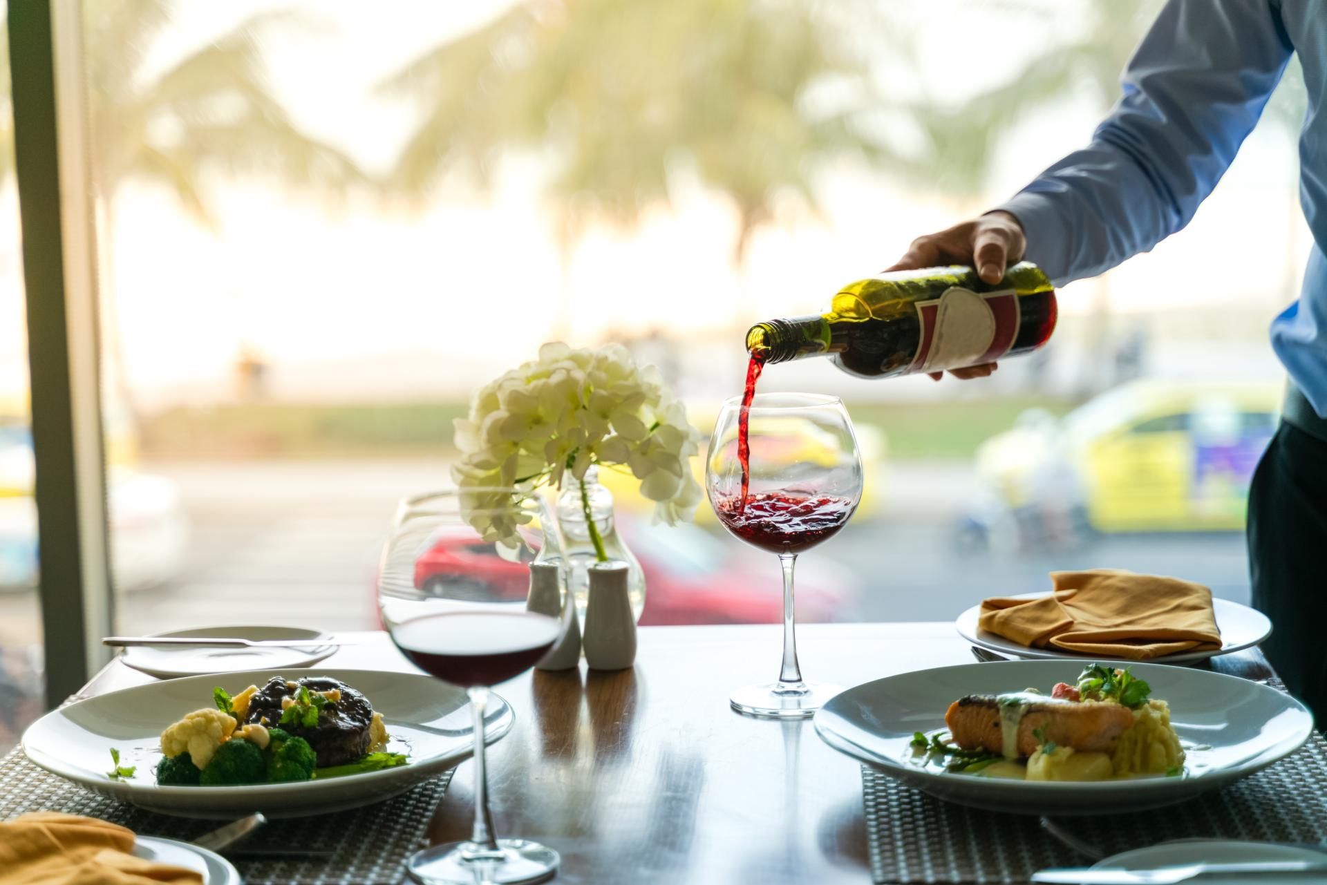 A man is pouring wine into a glass at a restaurant.