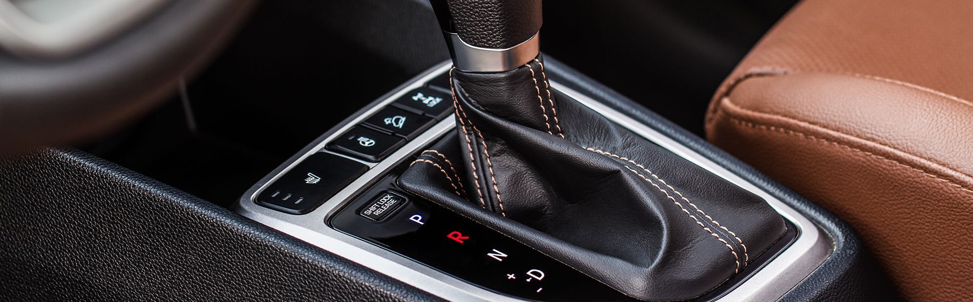 Close-up of a car's automatic transmission gear selector with leather trim and various buttons.