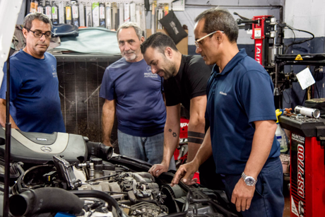 A group of men are working on a car engine in a garage.