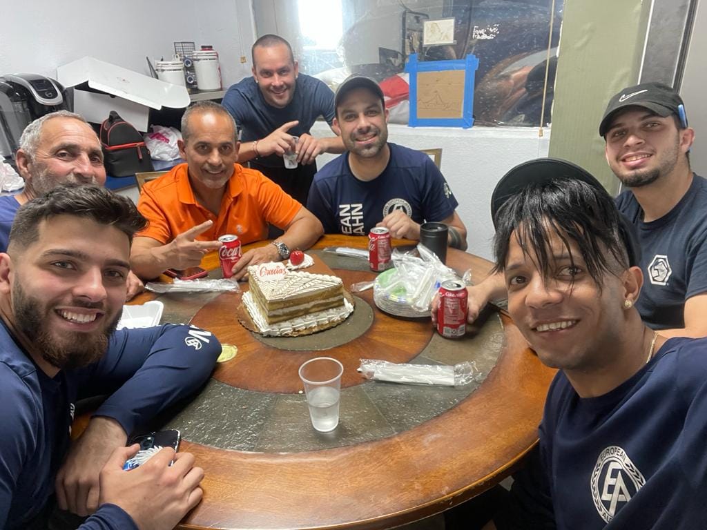 A group of men are sitting around a table with a cake on it.